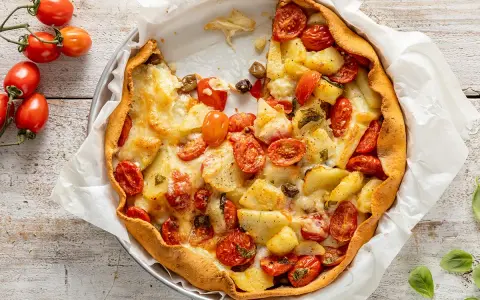 Torta salata con patate, pomodorini e formaggio filante, un piatto rustico e gustoso, pronto per essere gustato.