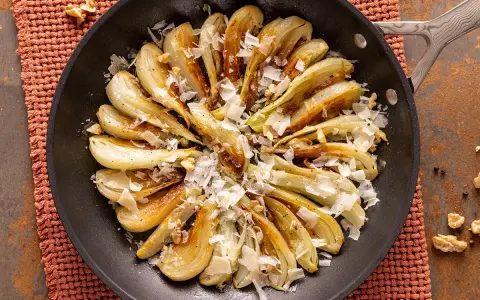 Finoçchi gratinati in padella, dorati e profumati, con scaglie di parmigiano e noci croccanti.