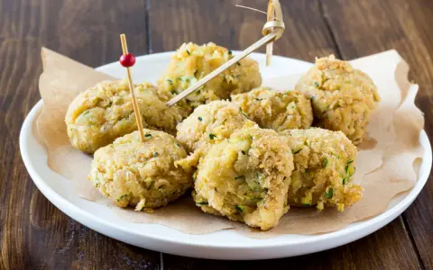 Polpette di ceci e zucchine dorate e croccanti, servite su un piatto bianco con stuzzicadenti decorativi.