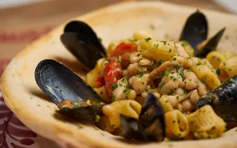 Un piatto invitante di pasta fagioli e cozze, con pomodorini e prezzemolo fresco, servito in una ciotola di pane croccante.
