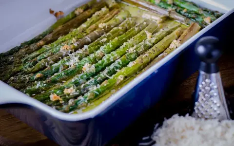 Asparagi al forno dorati e saporiti, conditi con formaggio grattugiato e pepe nero, pronti per essere gustati.