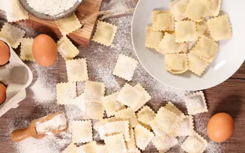 Tanti ravioli fatti in casa sparsi su un tavolo di legno, con farina, uova e una paletta.