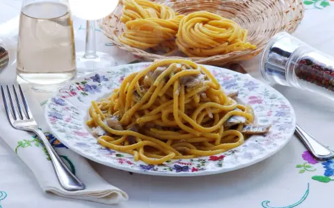 Un piatto di bigoli in salsa, con pasta fresca, acciughe e cipolla, pronto per essere gustato.