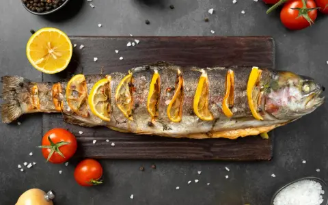 Un succulento pesce alla brace, guarnito con fette di limone e erbe aromatiche, pronto per essere gustato.