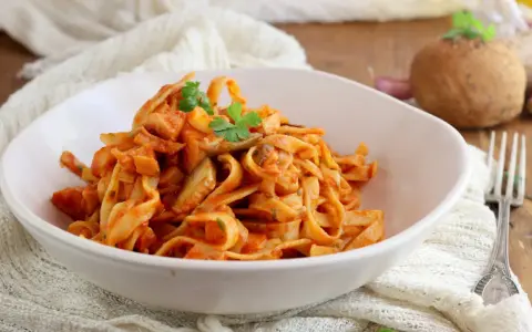 Un piatto invitante di tagliatelle ai funghi, condite con una ricca salsa al pomodoro e guarnite con prezzemolo fresco.