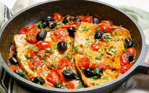 Pesce spada alla siciliana in padella con pomodorini, olive nere e capperi, guarnito con prezzemolo fresco.