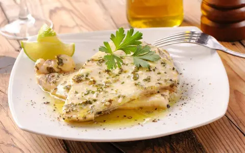 Delizioso pesce spada al forno, condito con erbe aromatiche e servito con spicchi di lime e prezzemolo fresco.