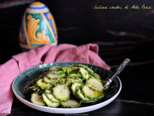 Fetta di zucchine marinate crude condite con erbe aromatiche e olio, servite su un piatto verde.