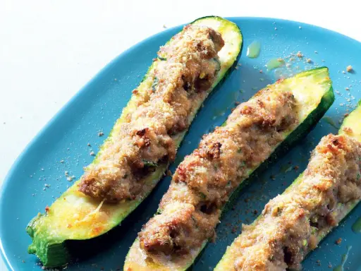 Tre zucchine ripiene, dorate e gratinate, servite su un piatto blu. Un piatto invitante e saporito.
