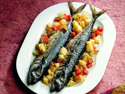 Due filetti di sgombro al forno, cotti alla perfezione, serviti con patate e carote a cubetti su un piatto bianco.
