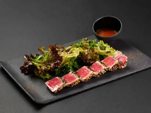 Tataki di tonno scottato, servito con insalata fresca e una ciotolina di salsa.