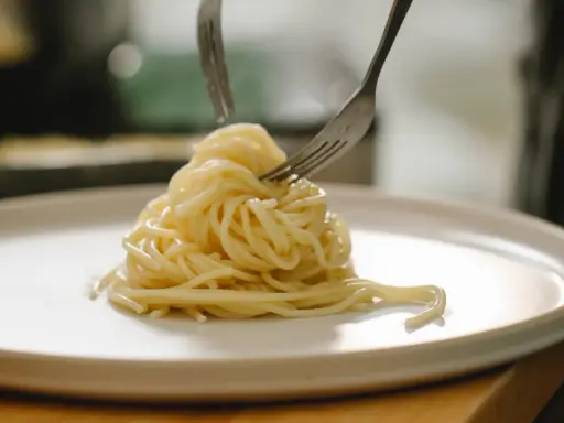 Spaghetti al limone serviti su un piatto bianco, con due forchette che raccolgono la pasta.