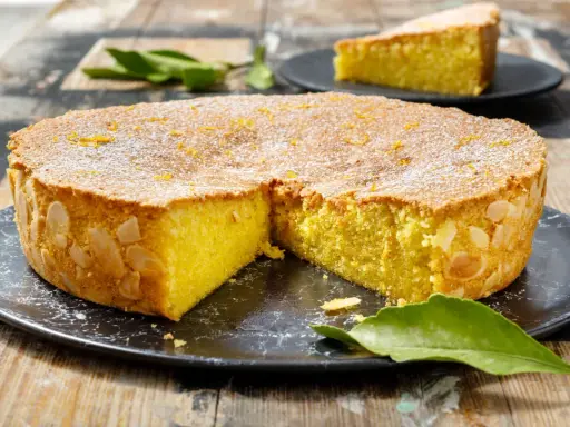 Deliziosa caprese al limone, con mandorle tostate sui bordi e scorzetta d'arancia in superficie, cosparsa di zucchero a velo.