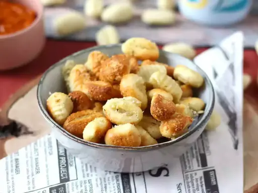 Gnocchi dorati e croccanti in friggitrice ad aria, serviti in una ciotola su carta di giornale.