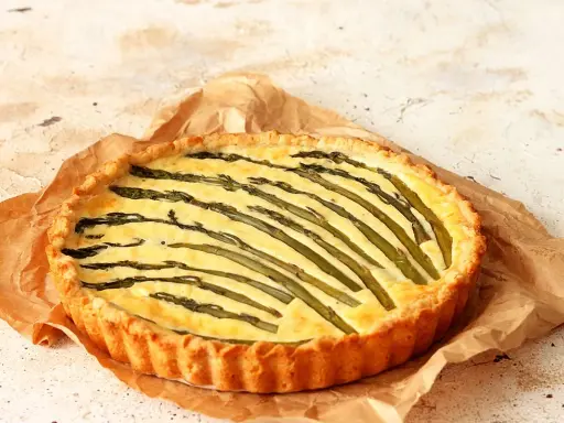 Torta salata asparagi con crosta dorata e ripieno cremoso, decorata con asparagi freschi disposti a raggiera.