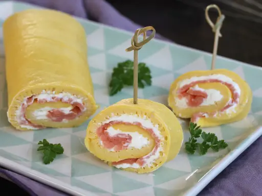 Rotolo di frittata ripieno di salmone affumicato e formaggio cremoso, guarnito con prezzemolo. Un antipasto elegante e gustoso.