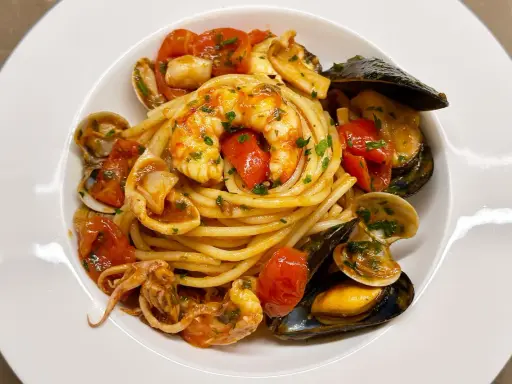 Un invitante piatto di spaghetti allo scoglio, con gamberi, cozze, vongole e calamari, condito con pomodorini e prezzemolo.