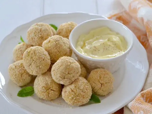 Polpette di ceci al forno dorate e croccanti, servite su un piatto bianco con una ciotolina di salsa cremosa e foglie di menta.