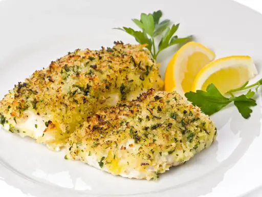 Delizioso merluzzo al forno con crosta croccante di erbe e pangrattato, guarnito con spicchi di limone e prezzemolo fresco.