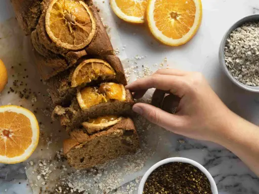 Un profumato plumcake all'arancia, uno dei tanti dolci senza glutine, pronto per essere gustato. Accanto, arance fresche e avena.