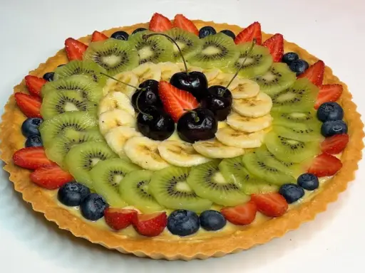 A fruit tart with kiwi, banana, strawberries, blueberries, and cherries on a custard filling.