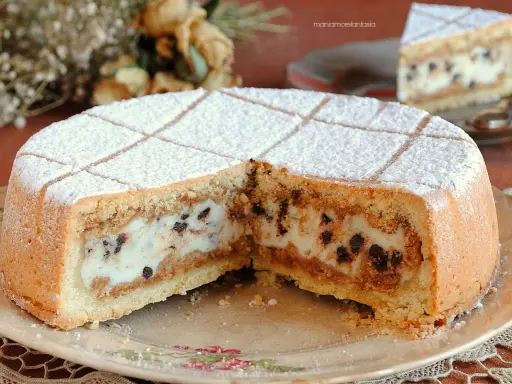 Una fetta di cassata al forno, con la sua crema vellutata e gocce di cioccolato, spolverata di zucchero a velo.