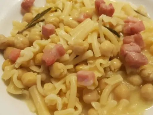 Un piatto di pasta e ceci in scatola, arricchito da cubetti di pancetta e un rametto di rosmarino.