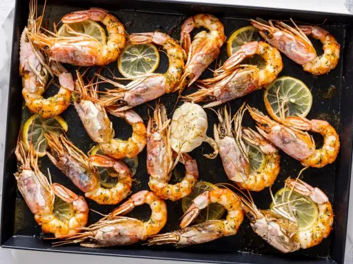 Gamberoni al forno dorati e succulenti, conditi con erbe aromatiche e spicchi di limone, pronti per essere gustati.