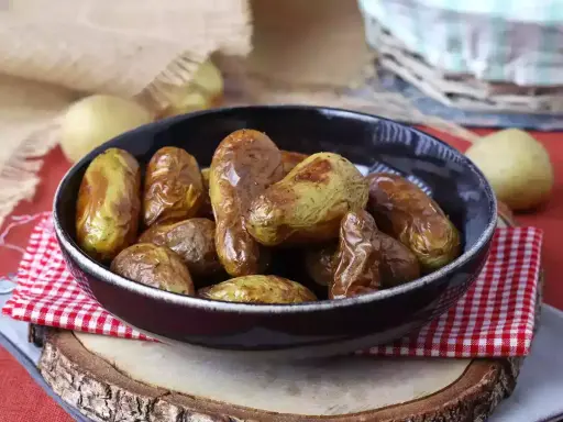 Patate novelle dorate e croccanti, appena sfornate dalla friggitrice ad aria, servite in una ciotola scura su un tagliere di legno.