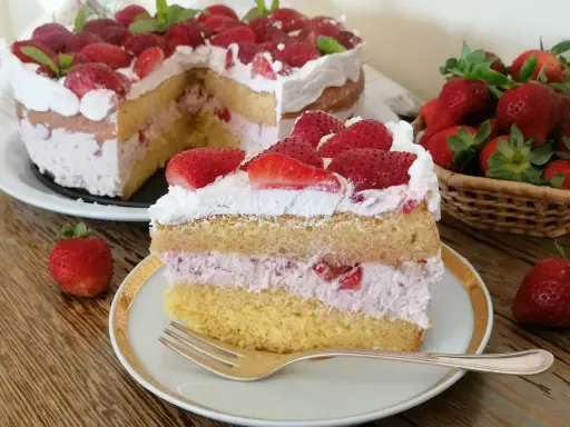 Una fetta di torta mascarpone e fragole, con strati di pan di spagna, crema rosa e fragole fresche, guarnita con panna e fragole.