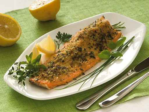 Deliziosa trota salmonata al forno, croccante e profumata, servita con limone e erbe aromatiche fresche.