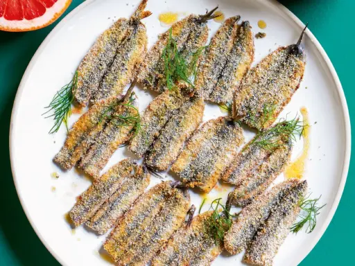 Piatto di alici al forno dorate e croccanti, guarnite con finocchietto fresco e un filo d'olio.