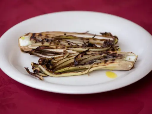 Radicchio in padella, grigliato e caramellato, servito su un piatto bianco con un filo d'olio.