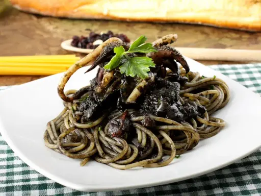 Un piatto invitante di spaghetti al nero di seppia, con tentacoli di calamaro e prezzemolo fresco, su una tovaglia a quadri verdi.