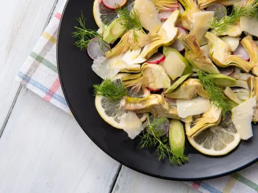 Un'insalata di carciofi crudi, con fette di limone, ravanelli e scaglie di parmigiano, guarnita con aneto fresco.