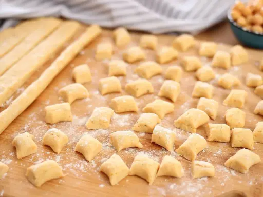 Piccoli gnocchi di ceci sparsi su un tagliere di legno, pronti per essere cotti.