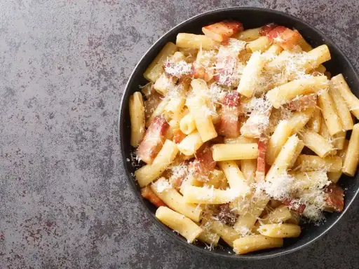 Un piatto di pasta alla zozzona fumante, con guanciale croccante e abbondante pecorino grattugiato, pronto per essere gustato.