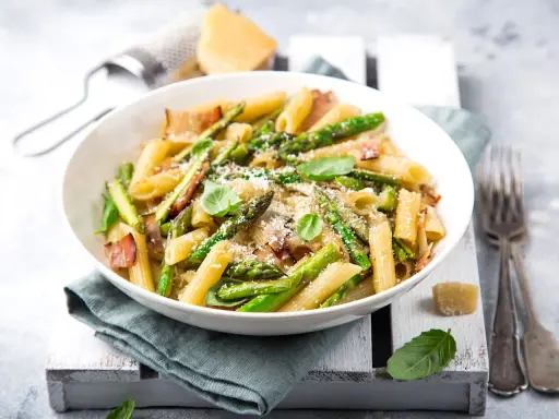 Piatto di pasta con asparagi e pancetta croccante, guarnito con basilico fresco e parmigiano grattugiato.