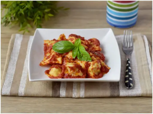 Un piatto di ravioli di carne conditi con sugo rosso e basilico fresco, pronti per essere gustati.