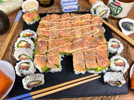 Un invitante sushi fatto in casa con salmone e avocado, guarnito con semi di sesamo e una salsa cremosa.