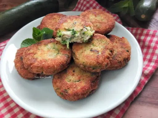 Piatto di polpette di zucchine e ricotta dorate e croccanti, guarnite con menta fresca.