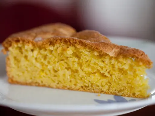 Una fetta di torta soffice e dorata, preparata con farina di mandorle, su un piatto bianco.