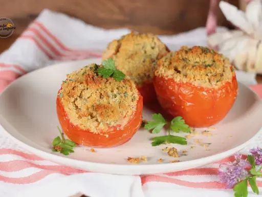 Tre pomodori gratinati al forno, ripieni e dorati, guarniti con prezzemolo fresco su un piatto bianco.
