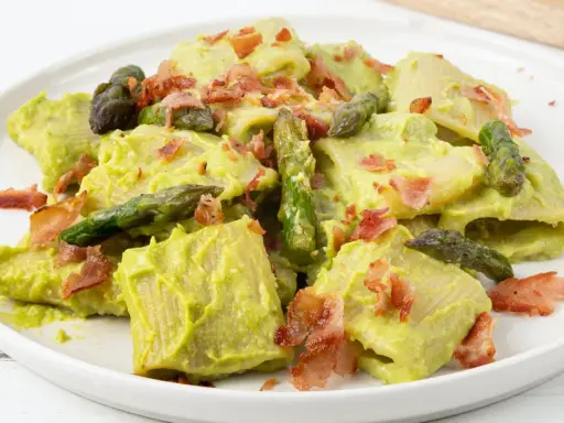 Piatto di pasta con crema di asparagi, punte di asparagi freschi e croccante speck.