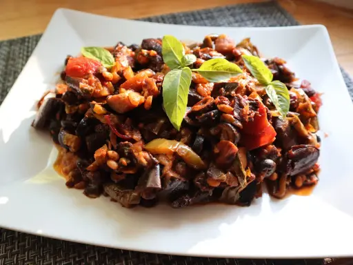 Un piatto di saporita caponata di melanzane, guarnita con foglie di basilico fresco.