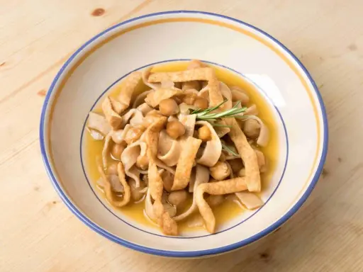 Piatto di ciceri e tria, pasta fresca con ceci e sfoglie fritte, guarnito con rosmarino.