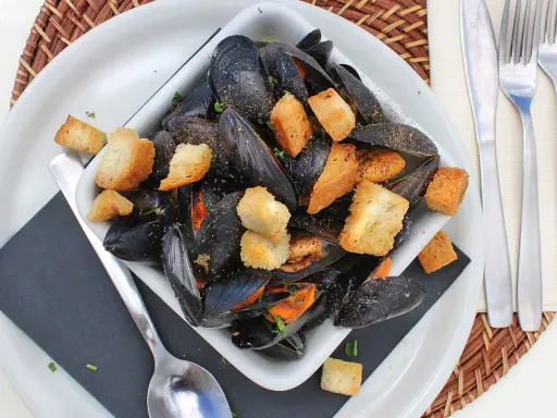 Un invitante piatto di impepata di cozze, ricco di molluschi neri e crostini dorati, pronto per essere gustato.