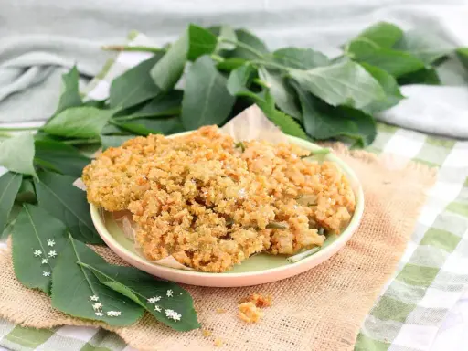Piatto di fiori di sambuco fritti, dorati e croccanti, guarniti con sale e accompagnati da foglie verdi e piccoli fiori bianchi.