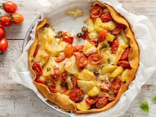 Torta salata con patate, pomodorini e formaggio filante, un piatto rustico e gustoso, pronto per essere gustato.