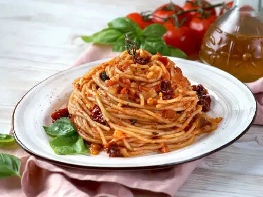 Spaghetti con pomodori secchi, basilico fresco e un filo d'olio d'oliva. Un piatto semplice e gustoso, pronto per essere assaporato.